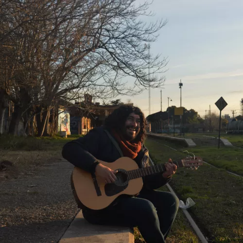 Hombre tocando guitarra al lado de vias del tren 