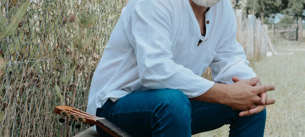 mauri sentado en un banco en el campo con su guitarra a un lado