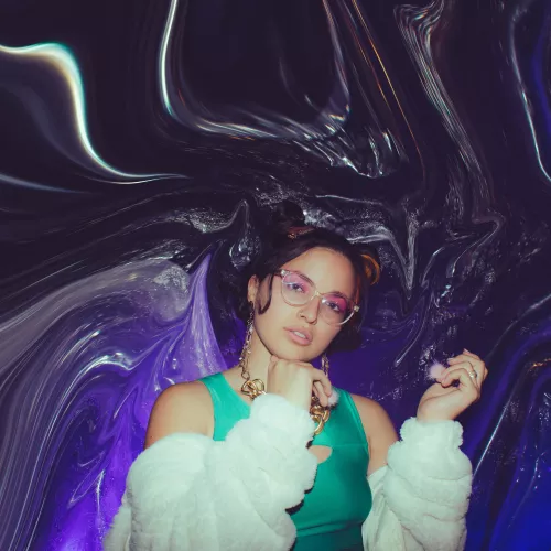 Foto con flash. Agus Acu en el centro de la imágen vestida de verde metalizado y mangas blancas de peluche, con fondo violeta oscuro de plástico derretido