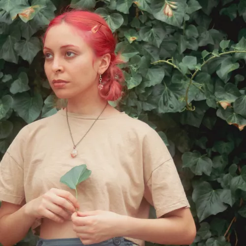 Mujer joven de pelo rosa mira hacia un lado mientras sostiene una hoja de árbol