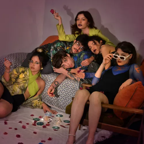Helen y Las gemas mirando a cámara , Las Gemas encimades entre si , Helen en un sofá aparte, hay flores por todo el suelo y encima de elles.
