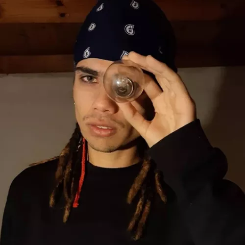 Keke NDK con rastas y una bandana en la cabeza, mirando a través de un foco