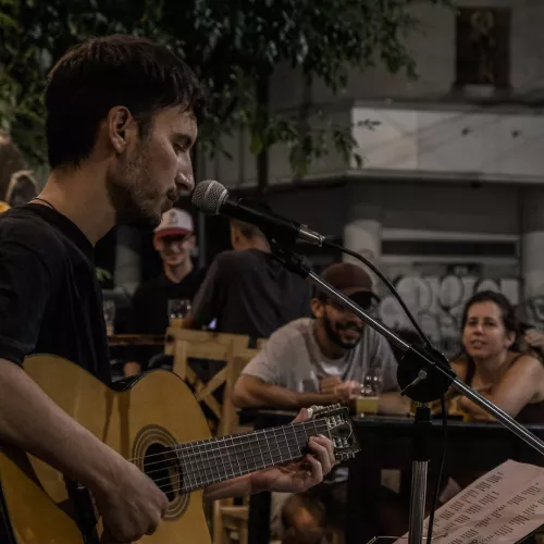 Foto de Nacho Meli con micrófono y guitarra criolla tocando ante público al aire libre.