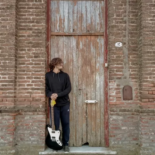 Nahu Elichiri, posando frente a casa antigua con guitarra eléctrica en mano