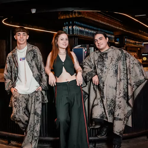 Retrato de tres jóvenes artistas en un bar moderno, iluminados por tonos cálidos, mostrando una estética urbana y segura antes de la filmación de un videoclip.