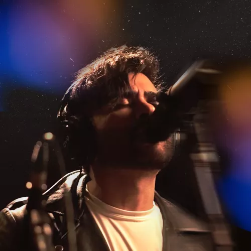 Artista Robyn Lekker cantando en un estudio de grabación con micrófono y auriculares, bajo iluminación artística.