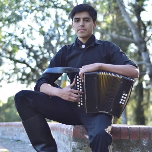 Santiago Torres con su acordeón dos hileras, ocho bajos, con un fundo de árboles verdes.