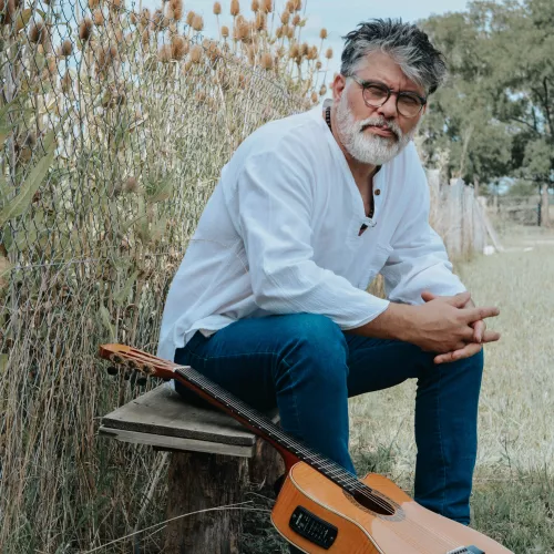 mauri sentado en un banco en el campo con su guitarra a un lado