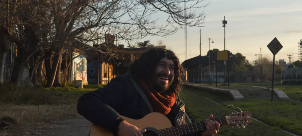 Hombre tocando guitarra al lado de vias del tren 