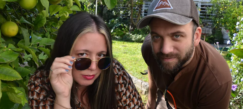 en un jardín, con un limonero y pasto de fondo, laura y gabriel miran a cámara.