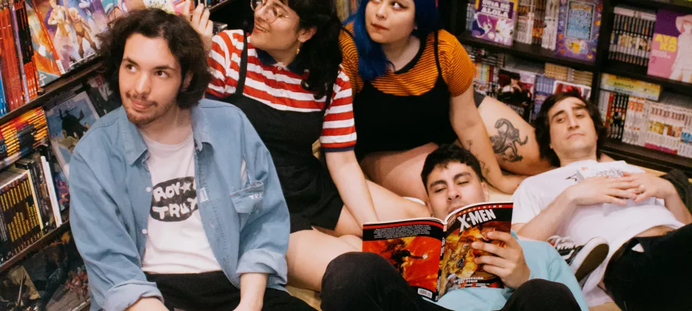 Un grupo de 2 chicas y 3 chicos sentados en el piso de un local de historietas leyendo y mirando cómics