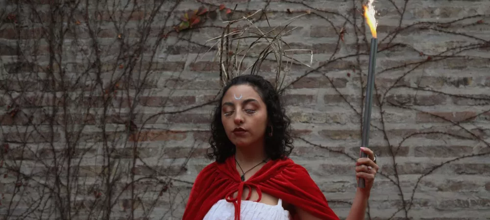 Foto del artista con una capa roja, una vara y un vestido blanco