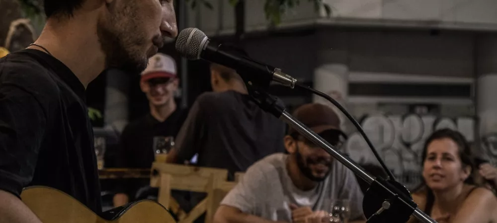 Foto de Nacho Meli con micrófono y guitarra criolla tocando ante público al aire libre.