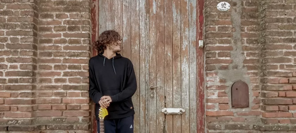 Nahu Elichiri, posando frente a casa antigua con guitarra eléctrica en mano