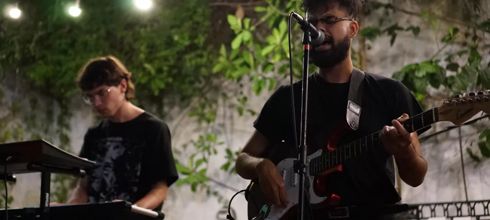 Dos personas paradas, una tocando el teclado, la otra cantando y tocando la guitarra.