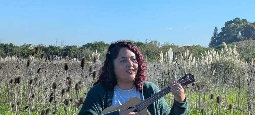 Se visualiza a la artista con un ukelele en un campo