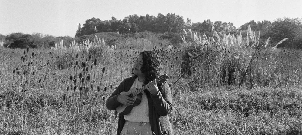 Se visualiza a la artista con un ukelele en un campo