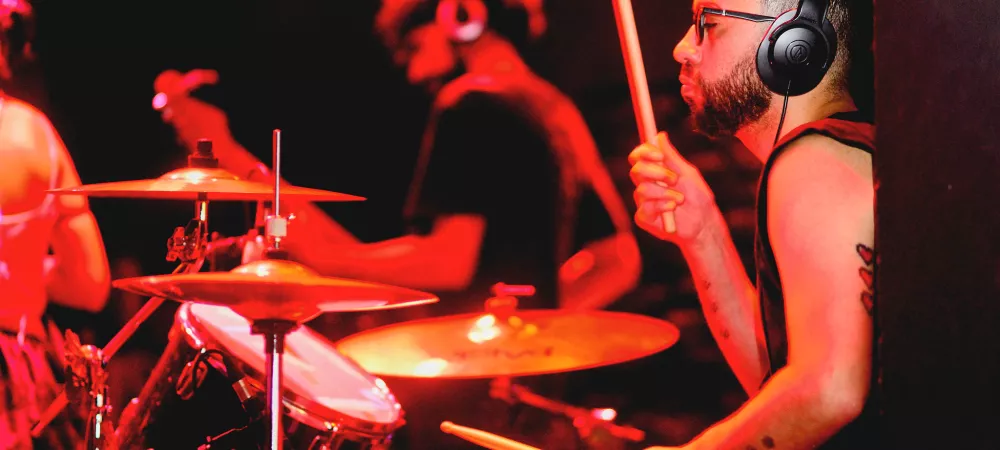 Imagen con tonos rojos que muestra a un baterista y un guitarrista tocando desde un lado