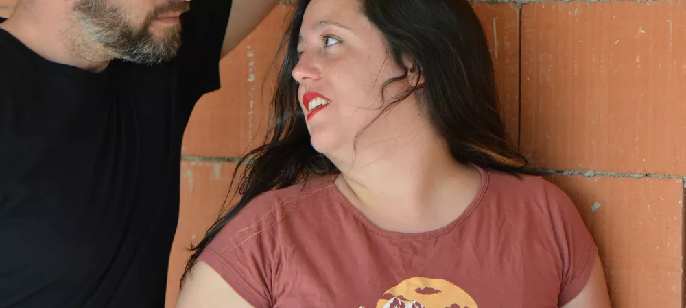 Con el fondo de una pared en construccion, a la izquierda esta gabriel y a la derecha laura, ambos se miran amorosamente.