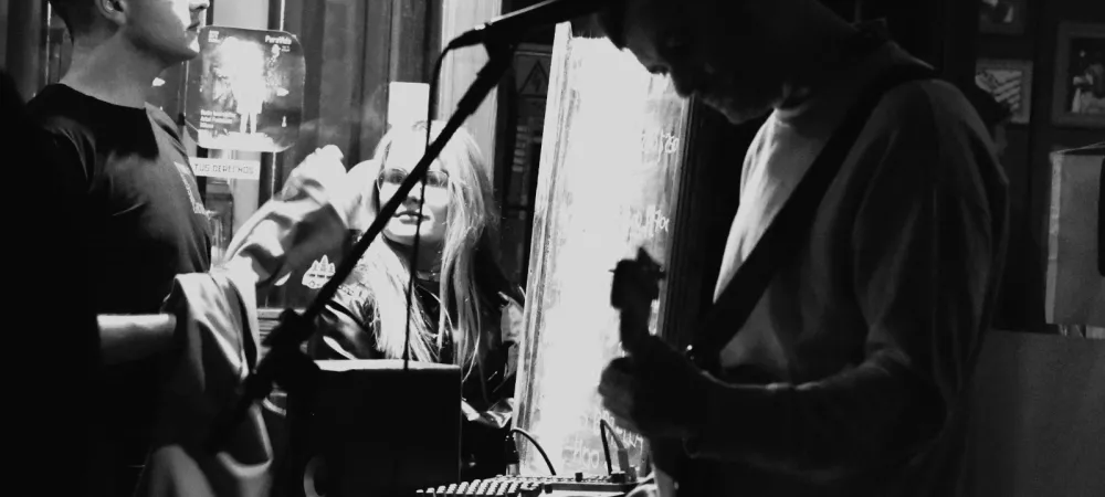 El músico tocando en una vereda, una chico mirando la escena de cerca y atrás, a través de una ventana, se ve a una chica en el interior de una bar