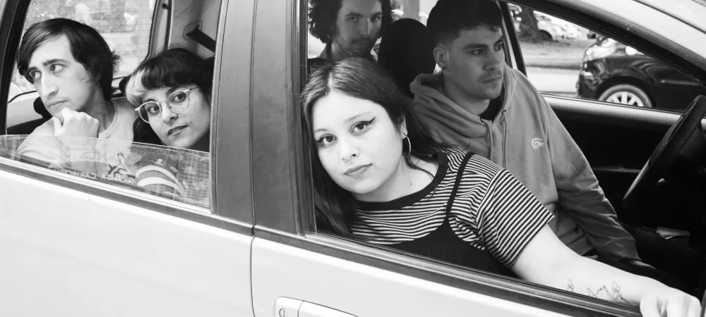 Un grupo de 2 chicas y 3 chicos mirando por afuera de las ventanas de un auto estacionado