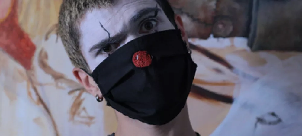 Keke NDK con maquillaje clown, y un barbijo negro con una nariz roja bordada