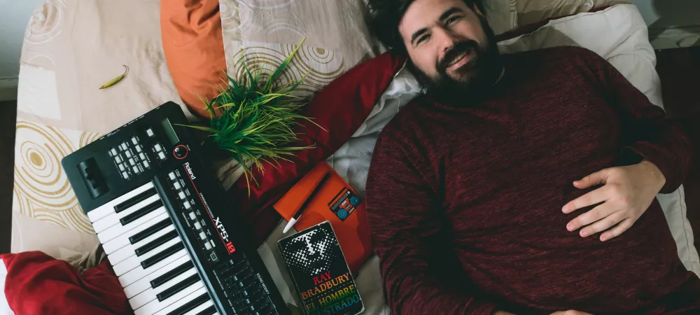 Yo acostado en un colchón. Alrededor mio objetos como libros, cuadernos y un teclado.