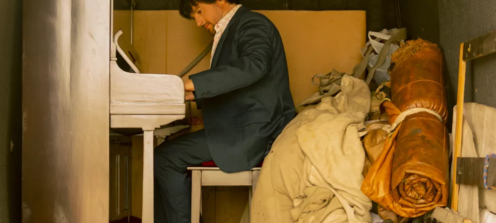 Ramiro Santos tocando un piano con concentración dentro de una camioneta, rodeado de objetos y telas.”