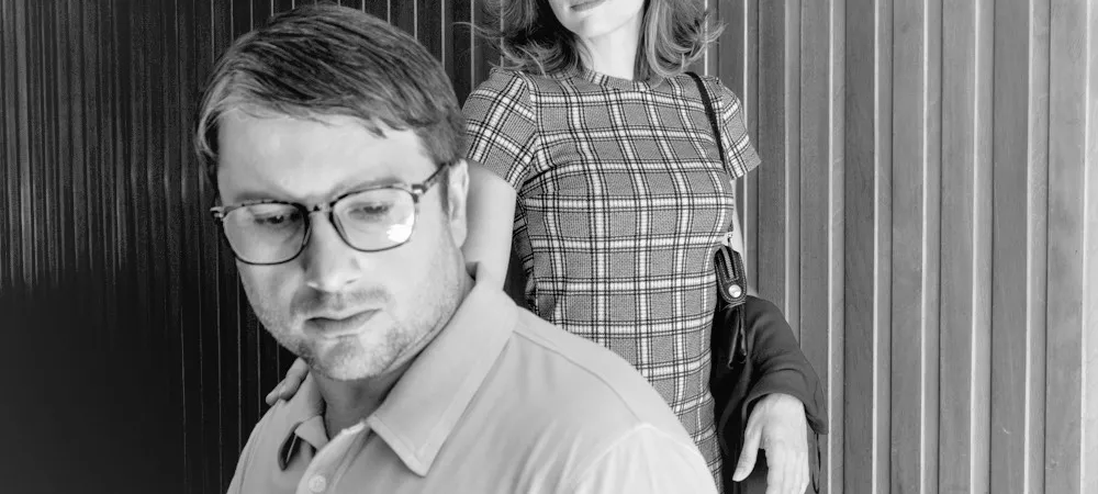 Ramiro Santos junto a una mujer en una escena ambientada en los años 60, frente a una pared de madera.